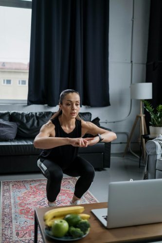 Žena radi čučnjeve u stanu dok gleda u laptop